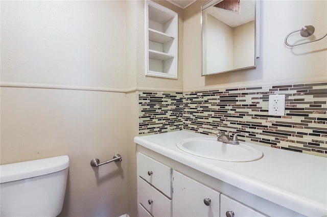 bathroom with tasteful backsplash, vanity, built in shelves, and toilet