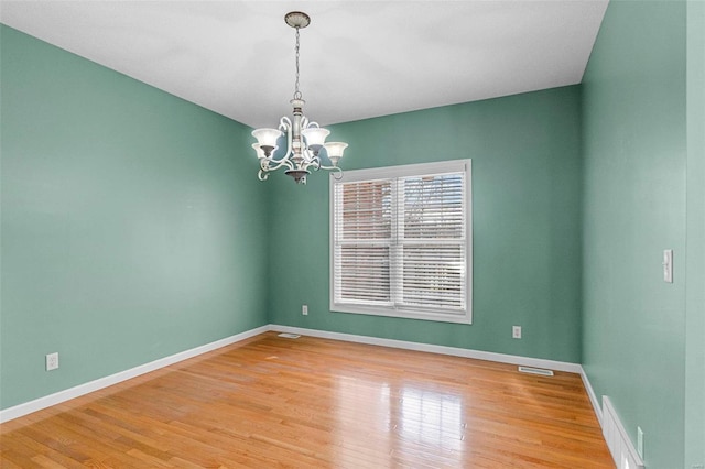 spare room featuring a notable chandelier and light wood-type flooring