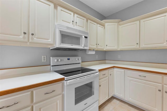 kitchen with light tile patterned flooring, cream cabinets, and white appliances