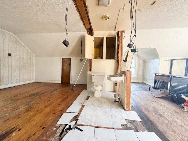 additional living space featuring hardwood / wood-style flooring, wooden walls, a textured ceiling, and vaulted ceiling