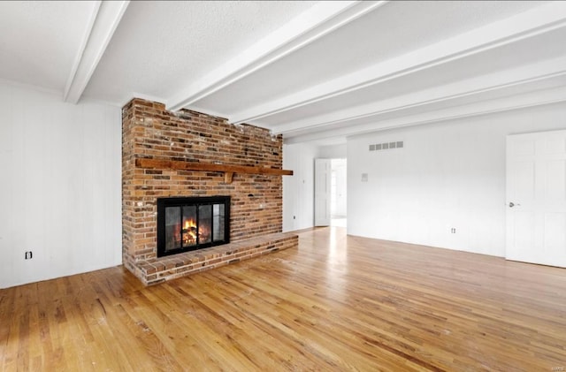 unfurnished living room featuring a brick fireplace, light hardwood / wood-style flooring, and beamed ceiling