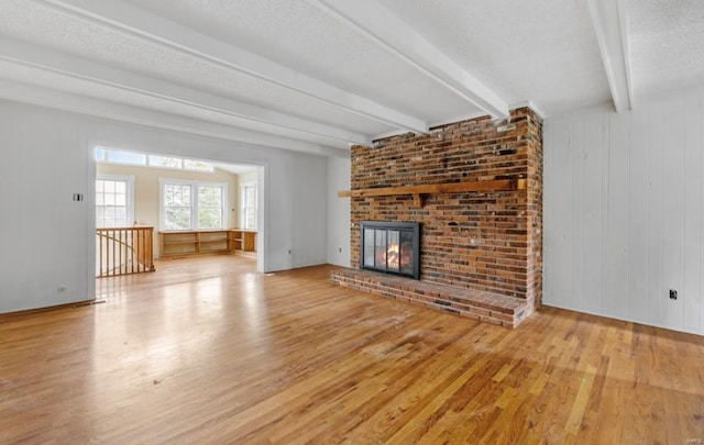 unfurnished living room featuring beam ceiling, a textured ceiling, a brick fireplace, and light hardwood / wood-style flooring