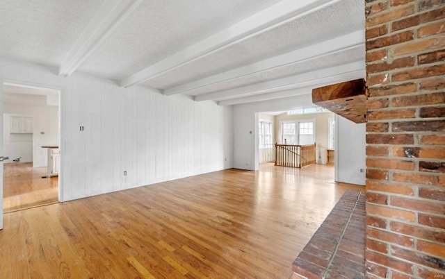 unfurnished living room with beam ceiling, a textured ceiling, and light hardwood / wood-style flooring