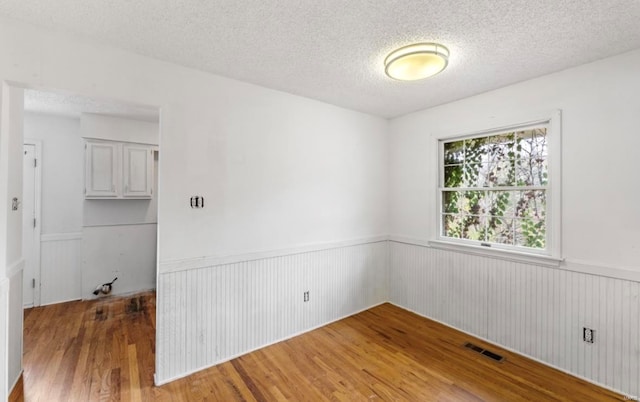 unfurnished room featuring hardwood / wood-style floors, wood walls, and a textured ceiling