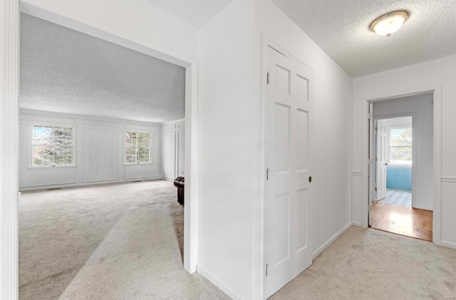 hall with a wealth of natural light, a textured ceiling, and light carpet