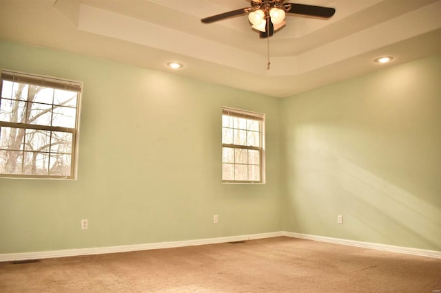 carpeted spare room featuring a tray ceiling and ceiling fan