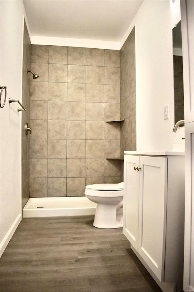 bathroom featuring hardwood / wood-style floors, vanity, toilet, and tiled shower