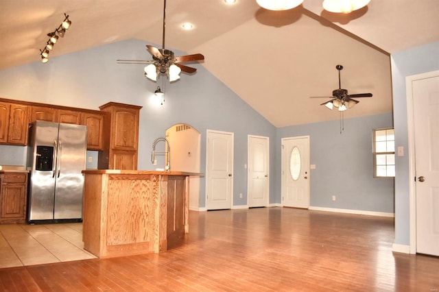 kitchen with a center island with sink, stainless steel fridge, light hardwood / wood-style floors, and high vaulted ceiling