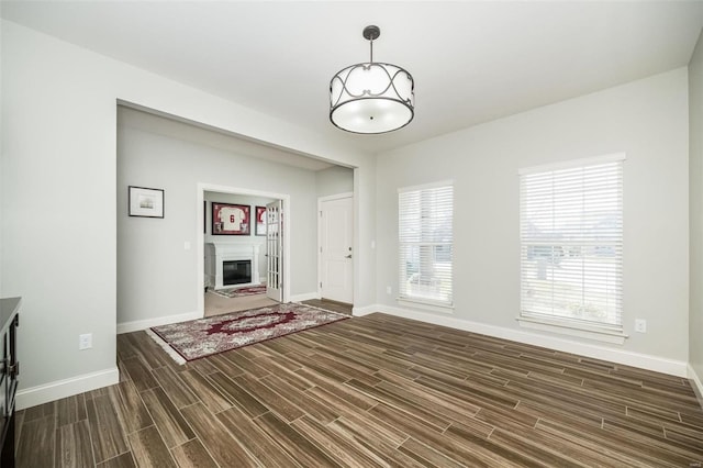 unfurnished living room with wood finish floors, a glass covered fireplace, and baseboards