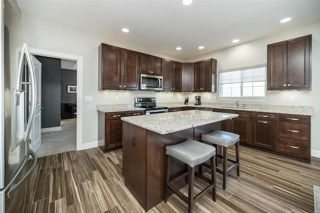 kitchen featuring a kitchen island, a breakfast bar, stainless steel appliances, wood finish floors, and recessed lighting