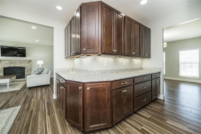 kitchen featuring wood tiled floor, baseboards, a stone fireplace, and recessed lighting