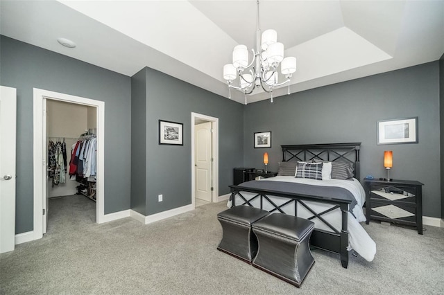 carpeted bedroom with a tray ceiling, a closet, a spacious closet, an inviting chandelier, and baseboards