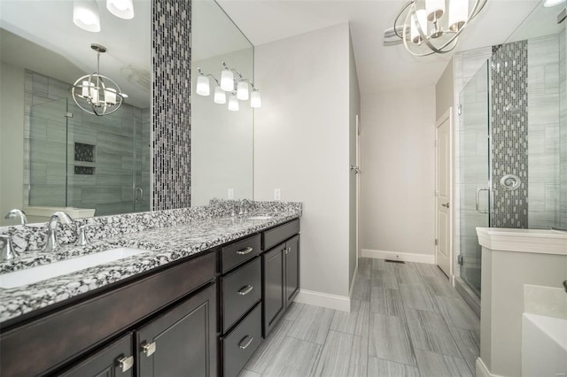 full bath with double vanity, a stall shower, a chandelier, and a sink