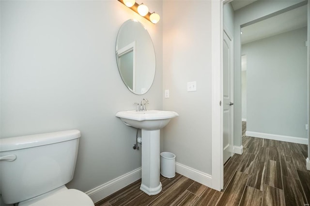 half bath featuring baseboards, toilet, and wood finished floors