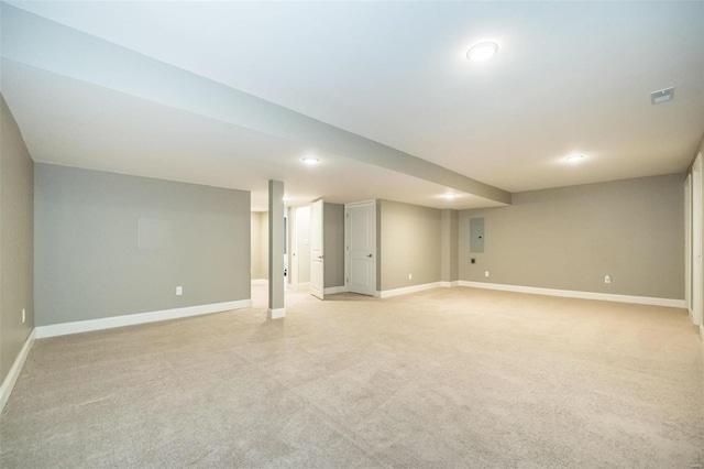 finished below grade area featuring light carpet, visible vents, electric panel, and baseboards