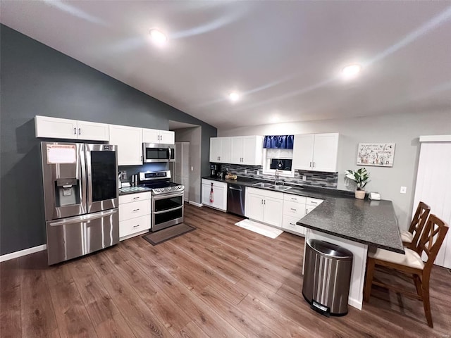 kitchen with a kitchen bar, appliances with stainless steel finishes, dark wood-type flooring, white cabinets, and lofted ceiling