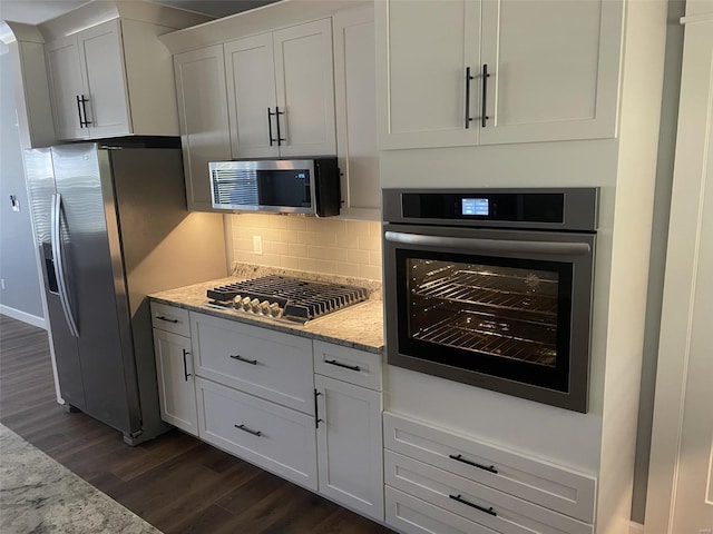 kitchen featuring appliances with stainless steel finishes, dark hardwood / wood-style floors, light stone countertops, decorative backsplash, and white cabinets