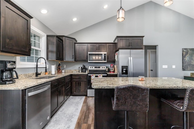 kitchen with appliances with stainless steel finishes, vaulted ceiling, hardwood / wood-style flooring, and a center island