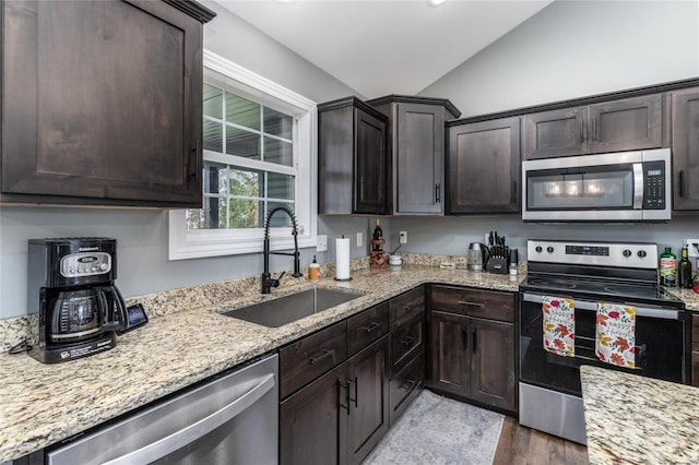 kitchen featuring light stone counters, stainless steel appliances, light wood-type flooring, sink, and lofted ceiling