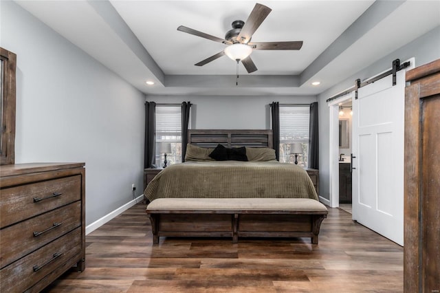 bedroom with a raised ceiling, a barn door, dark hardwood / wood-style floors, and ceiling fan