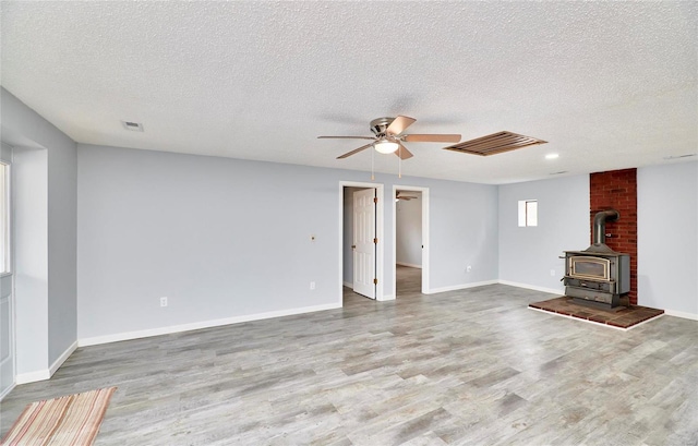 unfurnished living room with a textured ceiling, light wood-type flooring, and a wood stove