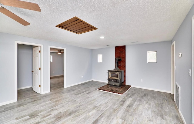 unfurnished living room featuring a textured ceiling, light wood-type flooring, and a wood stove