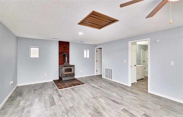 unfurnished living room featuring ceiling fan, light hardwood / wood-style floors, a wood stove, and a textured ceiling