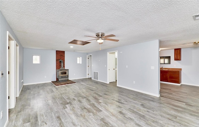 unfurnished living room featuring a textured ceiling, light hardwood / wood-style floors, and a wood stove