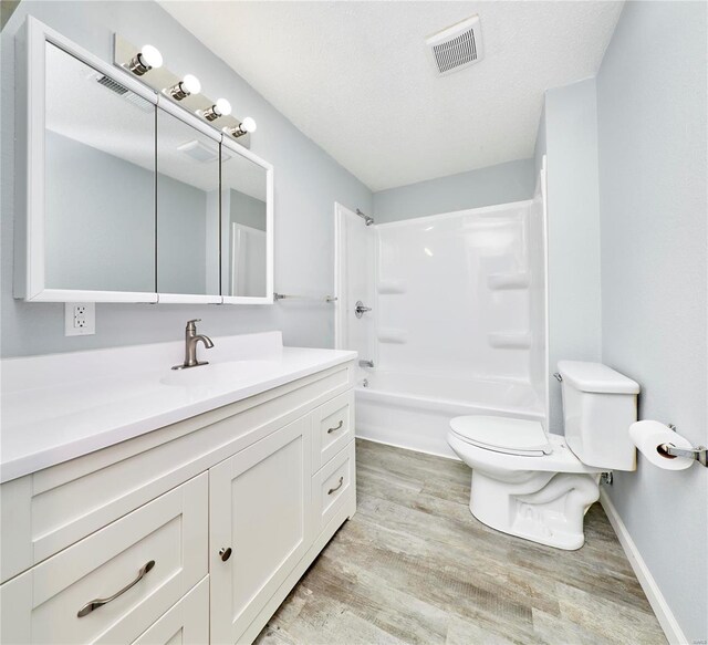 full bathroom with wood-type flooring, a textured ceiling,  shower combination, toilet, and vanity