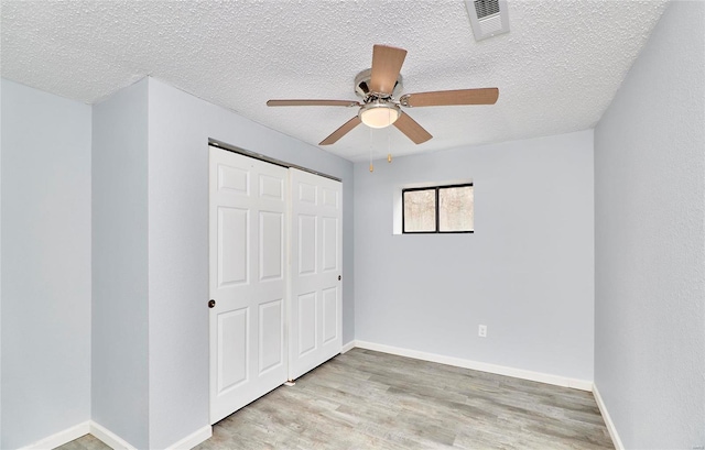 unfurnished bedroom with a closet, ceiling fan, light hardwood / wood-style flooring, and a textured ceiling