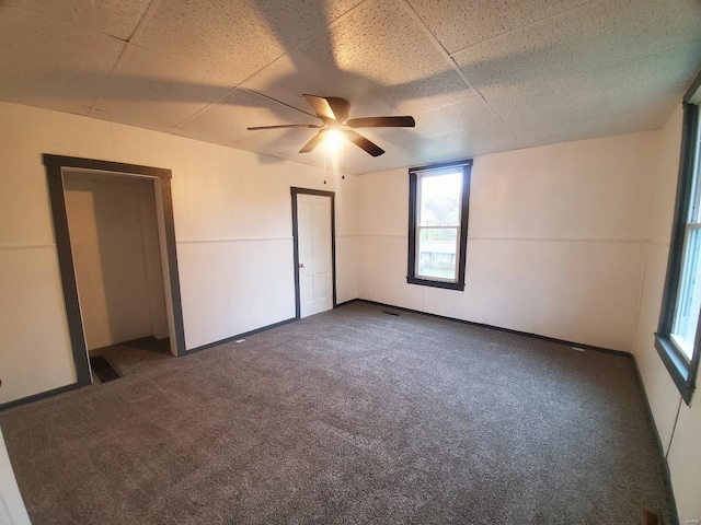 unfurnished room with ceiling fan and dark carpet