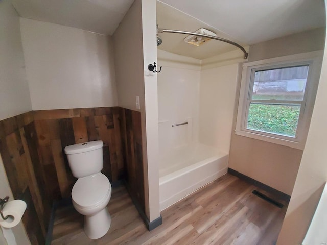 bathroom with hardwood / wood-style flooring, wood walls, shower / bathtub combination, and toilet