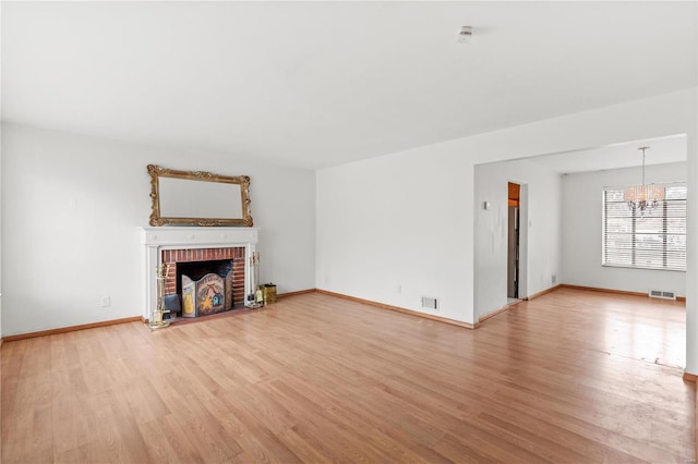 unfurnished living room featuring a fireplace, an inviting chandelier, and light hardwood / wood-style flooring