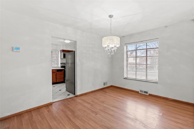 unfurnished dining area featuring an inviting chandelier and light wood-type flooring