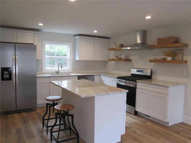 kitchen with white cabinets, light hardwood / wood-style flooring, wall chimney exhaust hood, a kitchen island, and stainless steel appliances