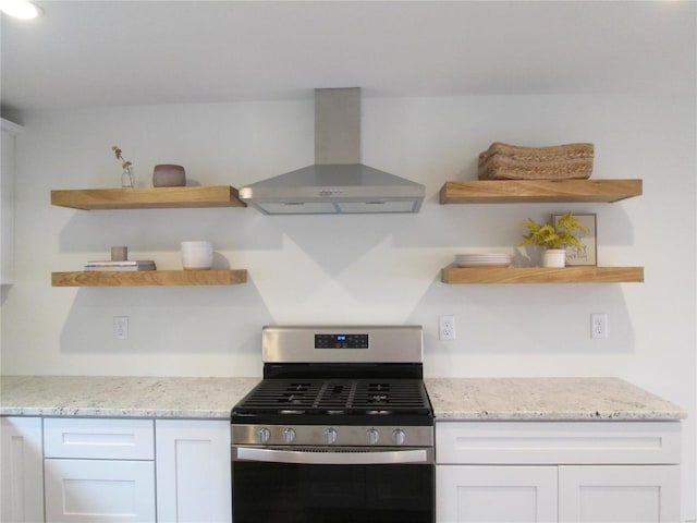 kitchen with light stone countertops, stainless steel gas stove, white cabinetry, and wall chimney exhaust hood