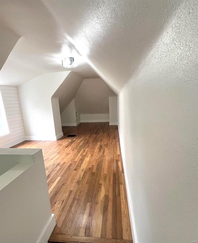 additional living space with a textured ceiling, hardwood / wood-style floors, and lofted ceiling