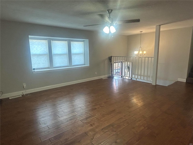 empty room featuring ceiling fan with notable chandelier and dark wood-type flooring