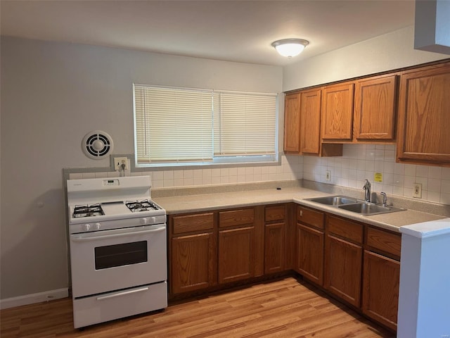 kitchen with decorative backsplash, light hardwood / wood-style flooring, white gas range, and sink