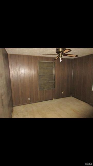 unfurnished room featuring ceiling fan and wood walls