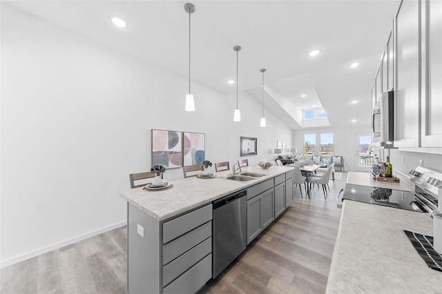 kitchen with stainless steel appliances, a kitchen island with sink, light hardwood / wood-style flooring, gray cabinetry, and pendant lighting