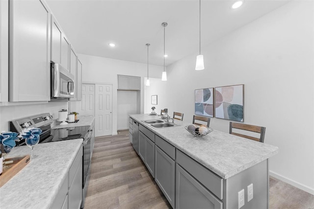 kitchen featuring a center island with sink, sink, appliances with stainless steel finishes, gray cabinets, and light wood-type flooring