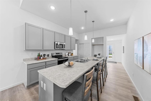 kitchen featuring stainless steel appliances, gray cabinetry, a kitchen island with sink, and decorative light fixtures