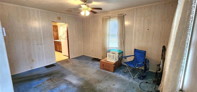 living area with ornamental molding, wooden walls, and ceiling fan