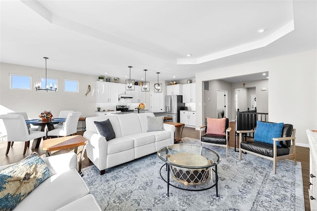 living room featuring a tray ceiling, a chandelier, and light hardwood / wood-style flooring