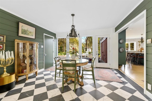 dining room featuring a notable chandelier, wood walls, ornamental molding, and light hardwood / wood-style flooring