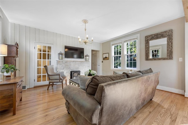 living room with a notable chandelier, a stone fireplace, ornamental molding, and light hardwood / wood-style flooring