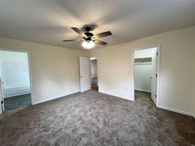 unfurnished bedroom with a walk in closet, dark carpet, ensuite bath, ceiling fan, and a closet