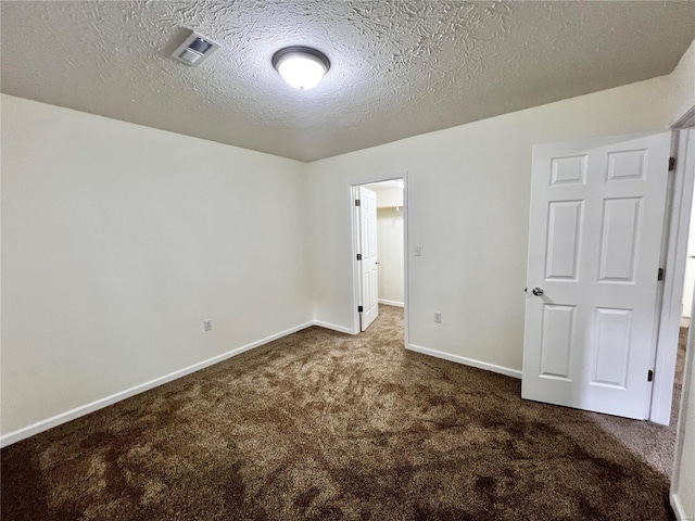 empty room with dark colored carpet and a textured ceiling