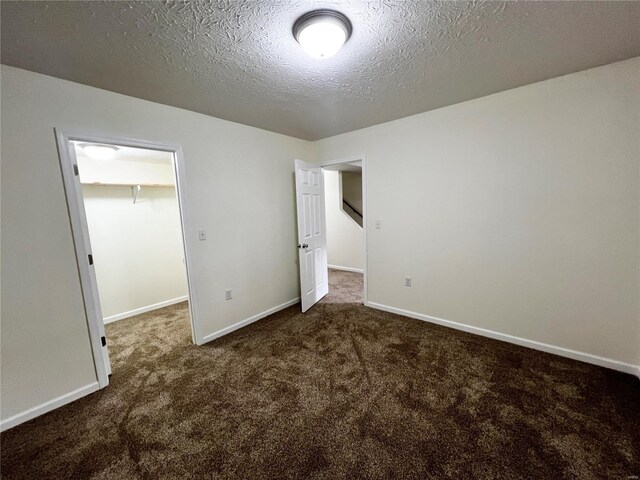 unfurnished bedroom with a walk in closet, a closet, a textured ceiling, and dark colored carpet